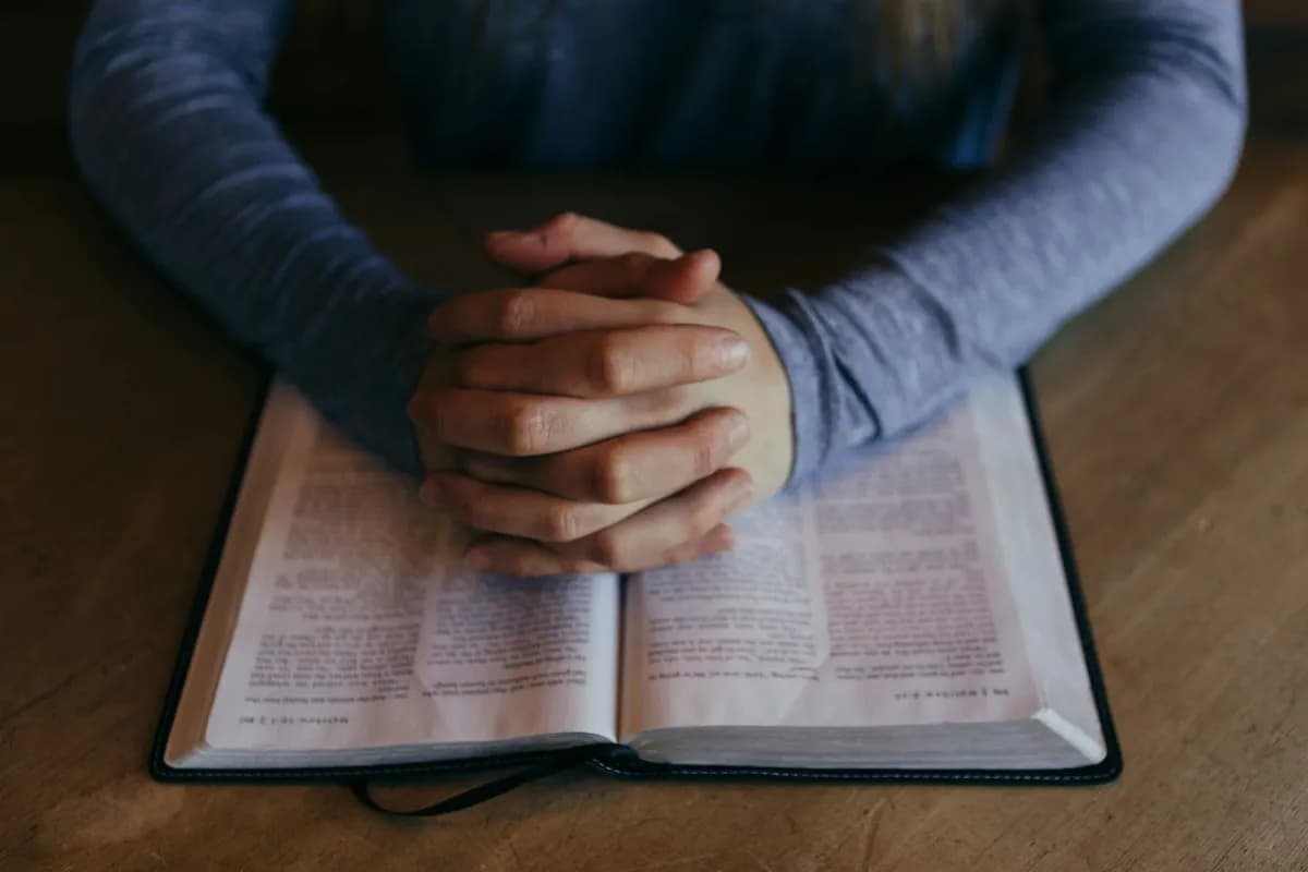 Hands praying over open Bible