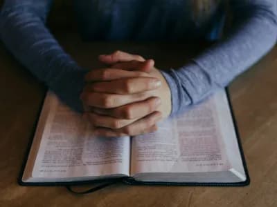 Hands praying over open Bible